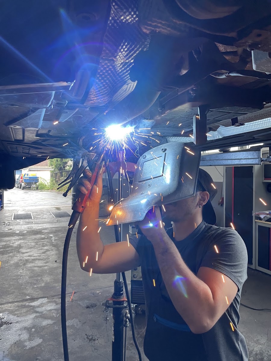 Mechaniker bei Schweißarbeiten unter einem angehobenen Fahrzeug in der Werkstatt von Anthoni Russo
